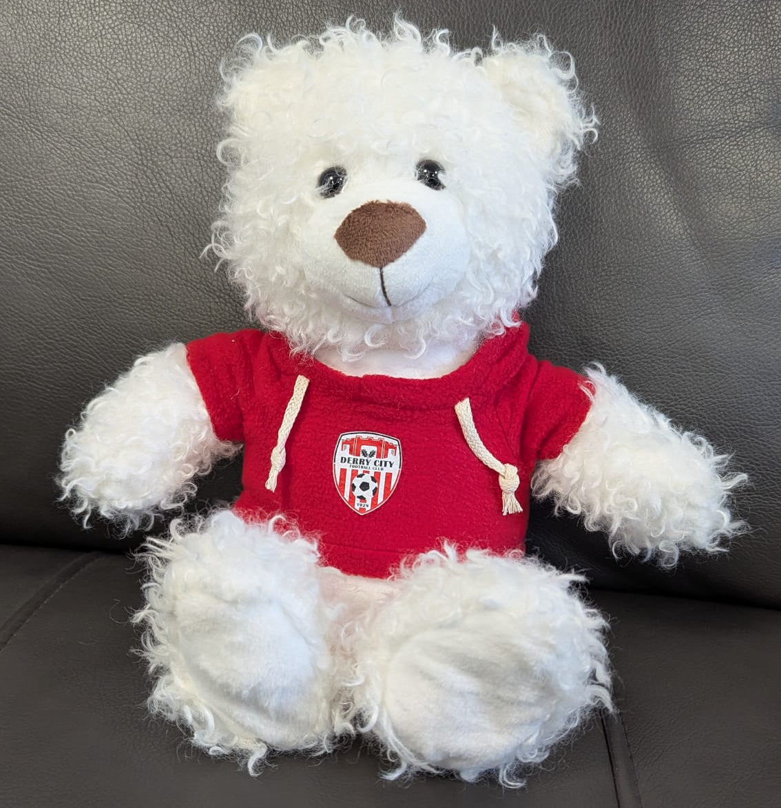 White teddy bear wearing a red shirt with a logo on a gray surface